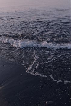 an ocean wave is coming in to shore on the beach at sunset or dawn,