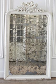 an old mirror sitting on the floor in front of a wall with peeling paint and white trim