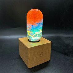 an orange and blue vase sitting on top of a wooden block in front of a black background