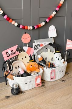 two white baskets filled with halloween items on top of a wooden floor next to a gray wall