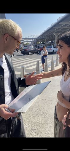 a man and woman standing next to each other in front of a parking lot talking