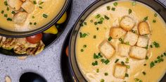 two black bowls filled with soup and croutons on top of a gray table