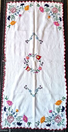 a white table cloth with colorful flowers and leaves on it, sitting on a black mat