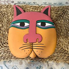 an orange and pink cat mask sitting on top of a wicker basket next to a rug