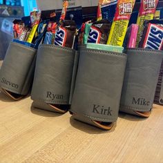 three gray leather pouches with candy and snacks in them sitting on a wooden table