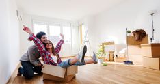 a man and woman sitting in a cardboard box on the floor with their feet up