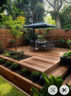 a wooden deck surrounded by plants and trees with an umbrella over the table in the middle