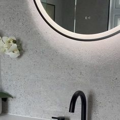 a bathroom sink sitting under a round mirror next to a vase with flowers on it