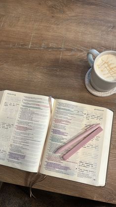 an open bible with a pink pen and cup of coffee on the table next to it