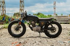 a black motorcycle parked on top of a dirt field next to a crane and trees