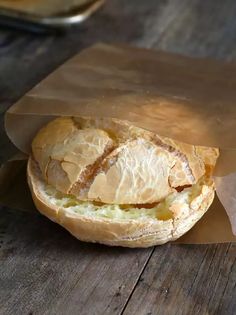 a sandwich wrapped in brown paper sitting on top of a wooden table