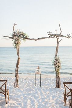 an outdoor ceremony set up on the beach with chairs and trees in the sand, overlooking the ocean