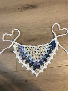 a crocheted blue and white bib hanging from a string on a wooden floor