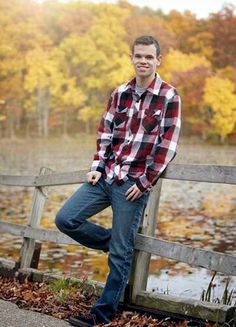 a man sitting on top of a wooden bench next to a body of water with trees in the background