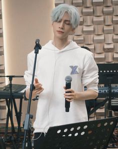 a man with blue hair is holding a microphone and standing in front of a keyboard