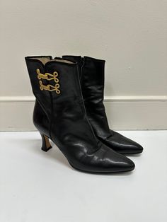 Black leather ankle boots with gold accent fasteners Materials: Leather Size: 7.5 Heel Height: 2 in Made in: Made in Mexico Gold Leather Boots For Evening, Formal Ankle Boots With Metal Feet, Gold Leather Evening Boots, Luxury Black Boots With Leather Trim, Crown Vintage Black Boots, Black Boots With Gold Chains, Gold Ankle Leather Heeled Boots, Black Boots Gold Hardware, Black Boots Gold Chain