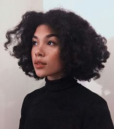 a woman with curly hair wearing a black turtle neck sweater and looking off to the side