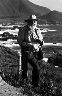 an old man standing on top of a hill next to the ocean