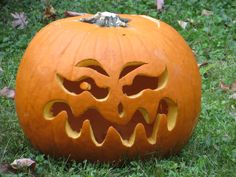 a carved pumpkin sitting in the grass with its mouth open