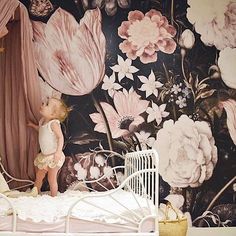 a doll standing on top of a bed in front of a floral wallpapered room