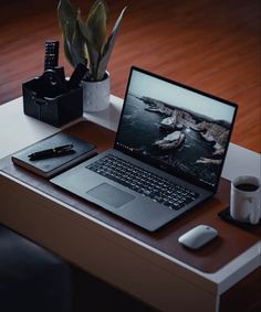 an open laptop computer sitting on top of a wooden desk next to a cup of coffee