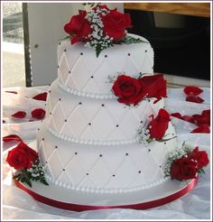 a three tiered wedding cake with red roses on the side and white icing