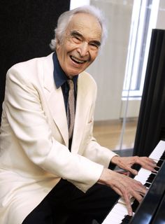 an older man sitting at a piano smiling