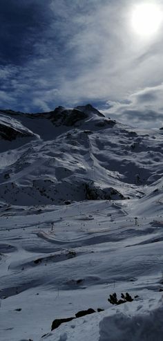 the sun shines brightly in the sky over snow covered hills and mountains on a cloudy day