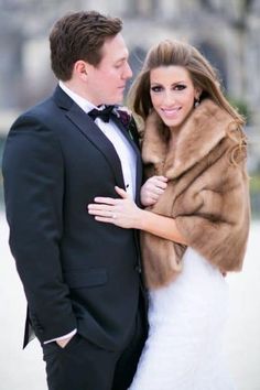 a bride and groom are posing for a photo in front of a building wearing fur stolers