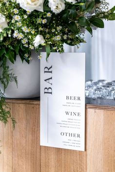 a bar sign sitting on top of a wooden counter next to flowers and wine glasses