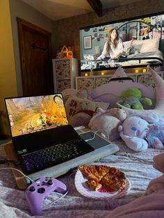 a laptop computer sitting on top of a bed next to a plate of pizza and a video game controller