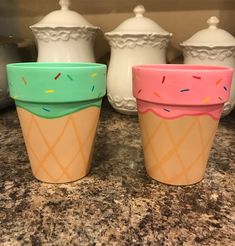 three ice cream cups with sprinkles painted on them sitting on a counter