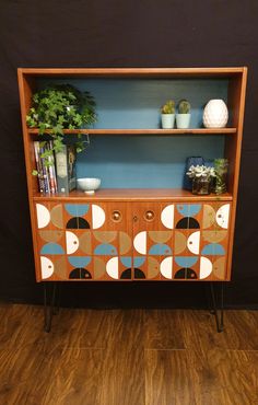 a wooden cabinet with an abstract design painted on the front and sides, along with potted plants