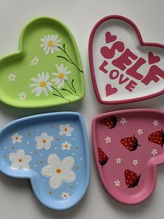 four heart shaped plates with flowers and butterflies painted on them, one has the word self love