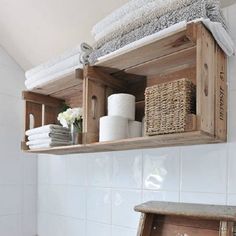 a wooden shelf filled with towels next to a white tiled bathtub and toilet paper