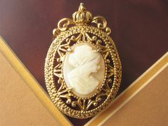 A beautiful signed Florenza cameo brooch, real carved shell portrait in an ornate goldtone setting with a crown at the very top. The backside has an attached bail if wanting to wear as a pendant by adding a necklace chain.  The brooch is 1 1/2 by 2 inch.  Mark:  Florenza In wonderful condition and ready to wear or give as a gift.  To see all the jewelry in my Etsy shop, go to my home page here ~ www.etsy.com/shop/darsjewelrybox Antique Gold Cameo Brooch, Antique Gold Cameo Brooches, Gold Cameo Brooch For Wedding, Gold Cameo Medallion Brooch, Gold Cameo Medallion Brooches, Elegant Gold Cameo Brooch, Gold Cameo Brooch Collectible, Formal Gold Cameo Brooches, Formal Gold Cameo Brooch