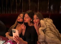 three women sitting at a table with one taking a selfie while the other holds up her phone