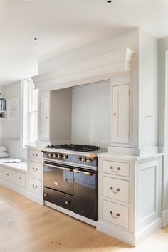 a kitchen with white cabinets and an oven in the center, along with hardwood flooring