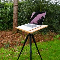 a laptop is sitting on top of a tripod in front of a tree and bushes