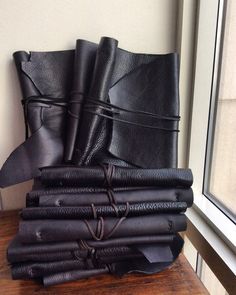 a stack of black leathers sitting on top of a wooden table next to a window