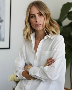 a woman standing with her arms crossed and looking at the camera while wearing a white shirt