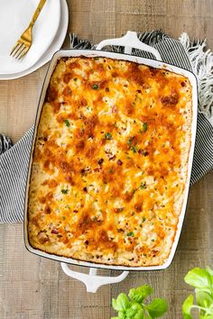 a casserole dish with cheese and herbs on a table next to a plate