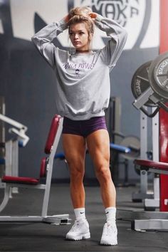 a woman standing in the middle of a gym with her hands on her head and one hand behind her head