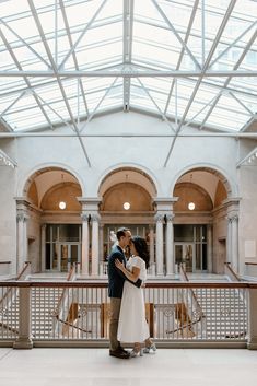 a man and woman standing in front of a building with glass roof over the walkway