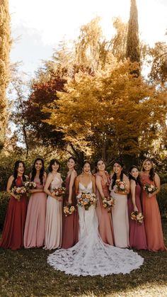 a group of women standing next to each other in front of some bushes and trees