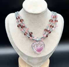 This piece is a graceful, layered heart shaped Andara Crystal necklace and sea bead necklace. The center heart piece has beautiful pink swirls. The colors are absolutely stunning. Colors are light pink to a pleasing purple and grey. This necklace is adjustable. Also, this necklace is lightweight and can be worn all day with ease. Will you add this to your collection? Will not be made again. Pink Beaded Heart Pendant Necklace, Pink Beaded Heart Pendant Jewelry, Pink Beaded Necklace With Heart Pendant As Gift, Pink Double Strand Necklace For Gift, Pink Heart Pendant Beaded Necklace For Gift, Pink Heart Pendant Beaded Necklace As Gift, Pink Heart Pendant Beaded Necklace For Valentine's Day, Pink Double Strand Beaded Necklace As Gift, Pink Multi-strand Jewelry Gift