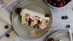 a piece of cake with white frosting and cherries on it next to two bowls of cherries