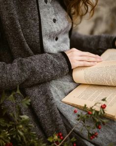 a woman sitting down reading a book with her hands on top of the open book