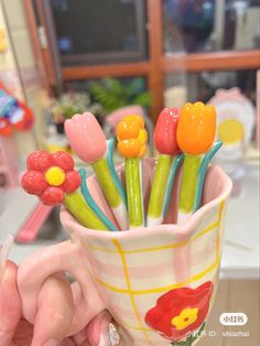 a hand holding a cup filled with plastic flowers