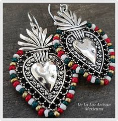 "Mexicana Earrings Materials:  Sterling Silver plated hooks, Silver plated heart, Glass Beads Length:  2.5\" The Mexicana Earrings are for those who love all things Mexico.  The country, the soccer team, the food... I could go on & on!  Inspired by Mexican Folk Art & the colorful embroidery crafted throughout Latin America.  I wrapped a vibrant blend of the Mexican Flag colors - Green, White, & Red around these gorgeous hearts.   The sacred heart is a symbol of everlasting love & commitment. You Mexican Flag Colors, Sacred Heart Art, Modern Mexican, Mexican Flags, Soccer Sports, Mexico Flag, Skull Sticker, Handcrafted Artisan Jewelry, Flag Colors